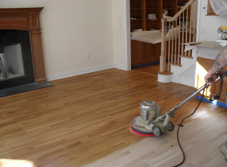 worker refinishing a wooden flooring of a house with white walls